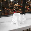 Weiße Elefanten-Duftlampe auf einer Fensterbank vor der beleuchteten Nächtlichen Skyline.