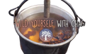 Ein dunkler, rustikaler metalltopf mit schwarzen griffen enthält simmernden amberfarbenen chaga tee aus chaga pilz inonotus obliquus