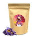 Ein beigefarbener, wiederverschließbarer Beutel mit Ancient Purity Blauer Lotusblume, gekennzeichnet mit einem leuchtenden purpur-roten Aufkleber. Ein kleiner Haufen getrockneter violett-blauer Lotusblüten liegt vor dem Beutel.