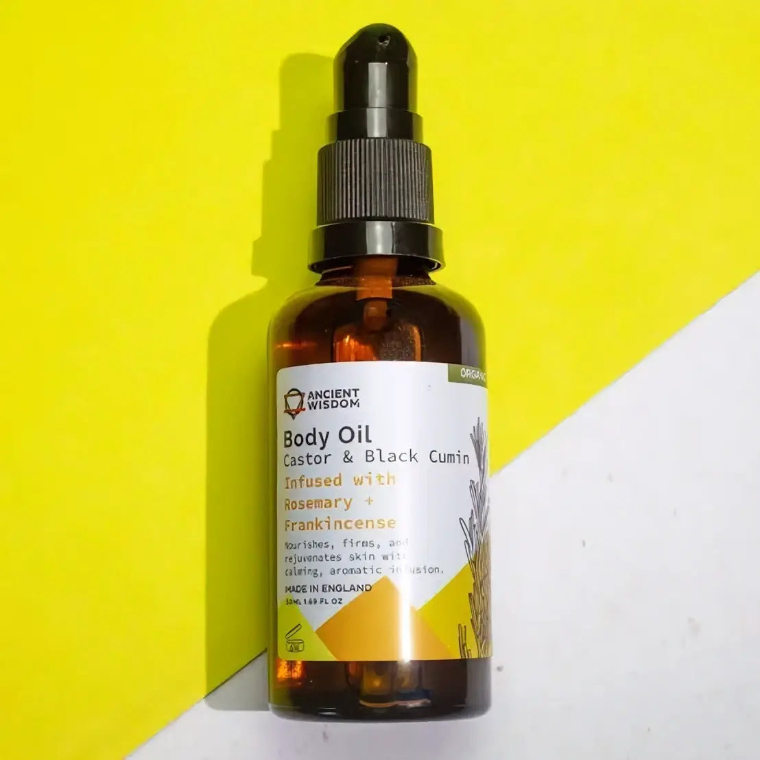 Eine bernsteinfarbene glasflasche ancient wisdom body oil rosmarin und weihrauch mit schwarzem tropfer und label