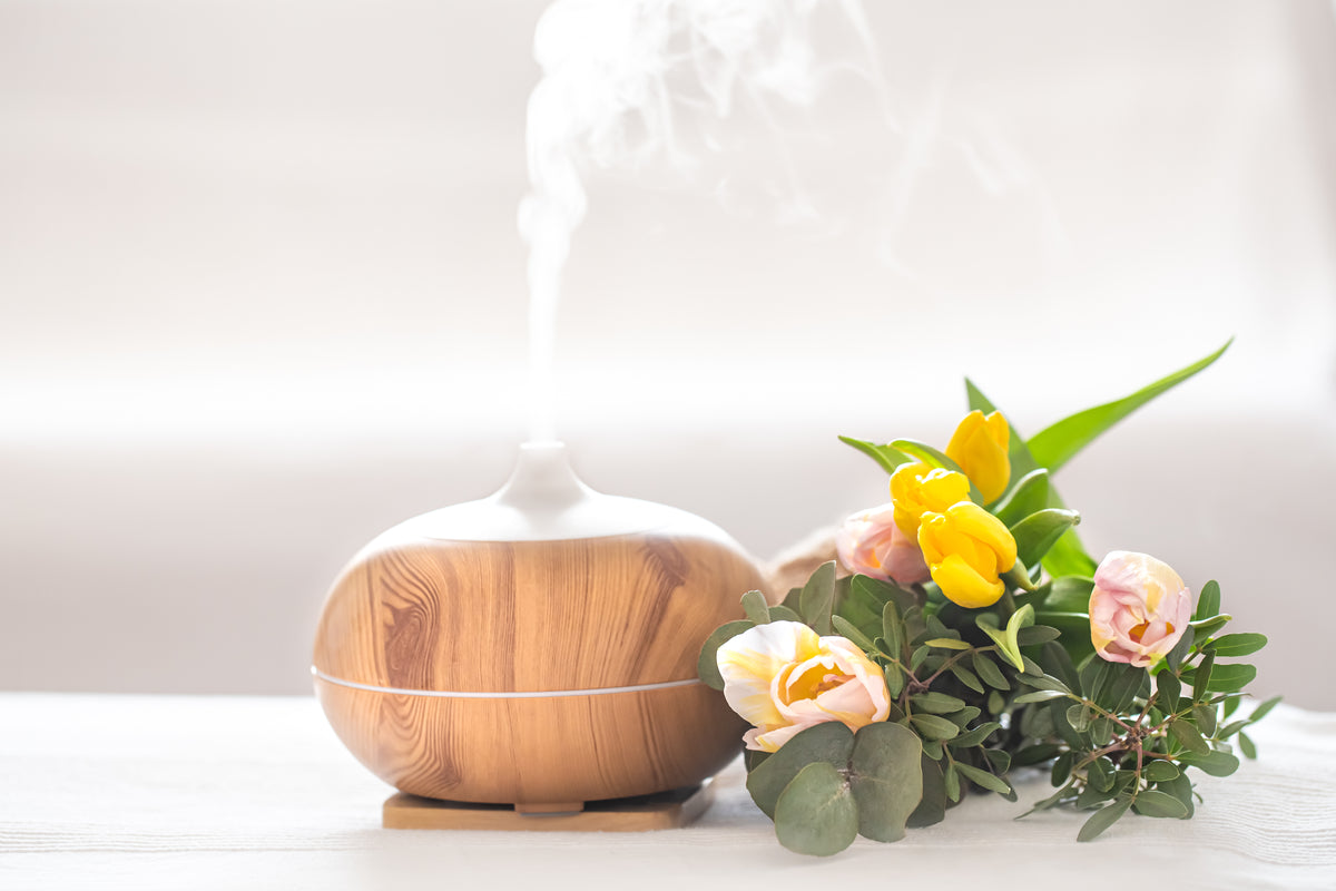 Holziger Aroma Diffuser mit aufsteigendem Dampf und gelben Tulpen auf hellem Tisch.