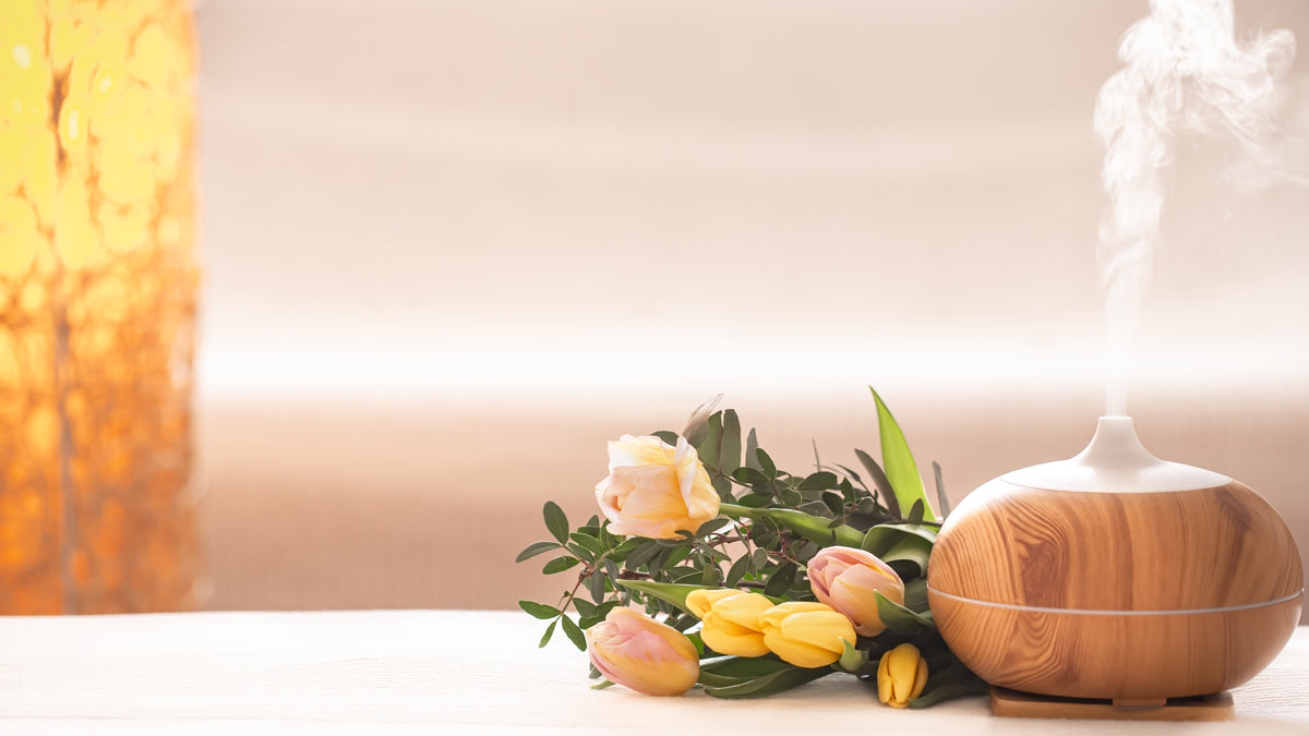Holz-Aroma Diffusor mit aufsteigendem Dampf und frischen gelben Tulpen auf hellem Tisch.