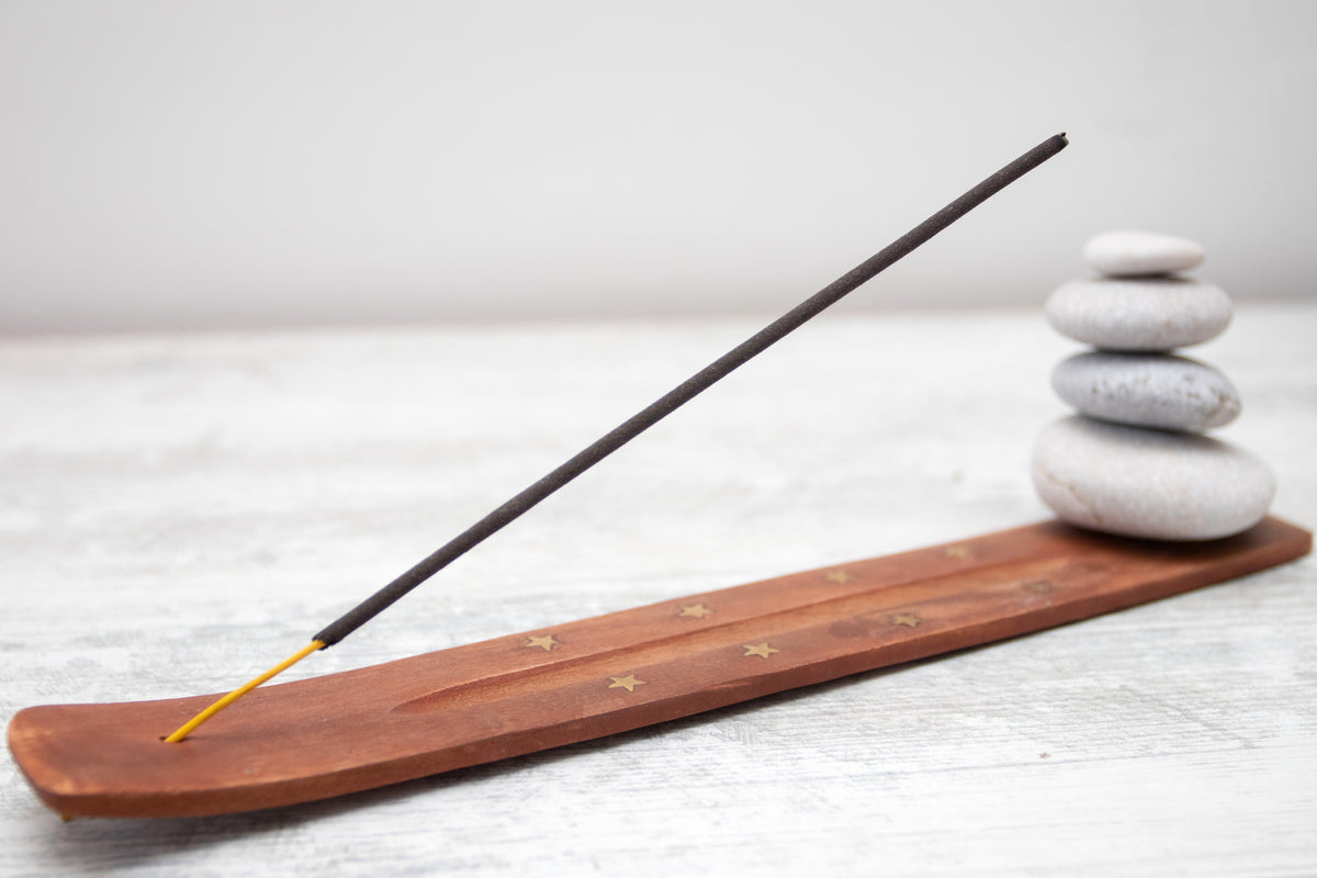 Holz-Räucherstäbchenhalter mit gestapelten Zen-Steinen auf hellem Untergrund.