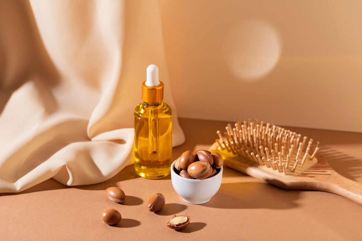 Bio Arganöl in Braunglas-Pipette mit Argan-Nüssen und Holzbürste auf beigem Stoff.
