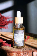 Ätherisches Lilith Öl von Ayamani Naturals mit Mondstein- und Tigeraugenkristallen, in einer Flasche auf einem Ritualtisch.