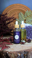Ätherisches Lilith Öl von Ayamani Naturals mit Mondstein- und Tigeraugenkristallen für feminines Ritual, Flasche auf natürlichem Hintergrund