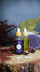 Ätherisches Lilith Oil Ritualöl von Ayamani Naturals mit Mondstein- und Tigeraugenkristallen, Flasche auf natürlichem Hintergrund