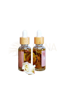 Zwei klare glasflaschen mit bambus-tropferkappen und pinken etiketten gefüllt mit goldenem ayamani naturals freya oil für bewusste rituale