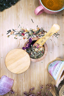 Ayamani Naturals Heart Chakra Grüntee mit Jasmin, Rose und Kräutern in einer Tasse mit frischen Blüten und Kräutern.