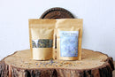 Zwei braune Kraftpapierbeutel mit "Throat Chakra" Balancing Tea stehen auf einer Holzscheibe eines Baumstumpfes.