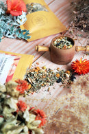 Ayamani Naturals Sakralchakra Kräutertee mit weiblicher Kräutermischung in einer Tasse, frische Kräuter und Blüten sichtbar