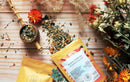 Ayamani Naturals Sakralchakra Kräutertee mit weiblicher Kräutermischung in einer Tasse, frische Kräuter und Blüten sichtbar