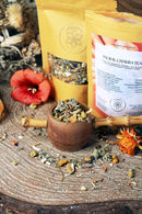 Ayamani Naturals Sakralchakra Kräutertee, weibliche Kräutermischung in einer Tasse mit frischen Kräutern und Teeblättern.