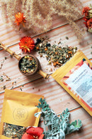 Ayamani Naturals Sakralchakra Kräutertee mit weiblicher Kräutermischung in einer Teekanne und Tasse, natürliche Zutaten sichtbar