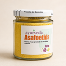 Ein klares Glas mit weißem Deckel, das 150g körniges braunes Asafoetida enthält. Das Etikett besagt, dass es ein in der orientalischen Küche geschätztes Harz und 100% natürlich ist.