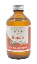 Ein bernsteinfarbenes glasfläschchen mit silbernem deckel und buntem etikett der marke rhyner enthält kapha aktivöl ayurvedisches massageöl bio 250ml