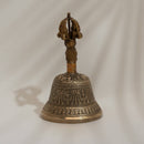 Eine Seitenansicht einer verzierten rituellen Messingglocke mit detaillierten traditionellen Gravuren auf einem schlichten Hintergrund.