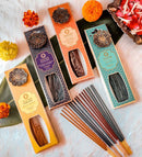 Vier senkrechte Schachteln Ayurveda Räucherstäbchen & Brenner, jeweils mit einem Messing-Blumenmedaillon. Die gezeigten Düfte sind: Tuberose Jasmin (Gelb), Lavendel Vetiver (Lila), Orange Minze (Orange) und Aqua Oud (Blau). Verschiedene Räucherstäbchen sind unten ausgebreitet.