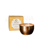 Ein gehämmerter kupfer kerzenhalter mit einer weißen kokosbutter und sojawachs vata tuberose jasmin duftkerze neben gelber ayurveda specialist verpackung