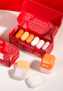 Eine rote Schachtel mit Blattmuster enthält sechs bunte Seifen in den Farben Orange, Rosa und Weiß. Drei Seifen sind ordentlich außerhalb der Schachtel angeordnet.