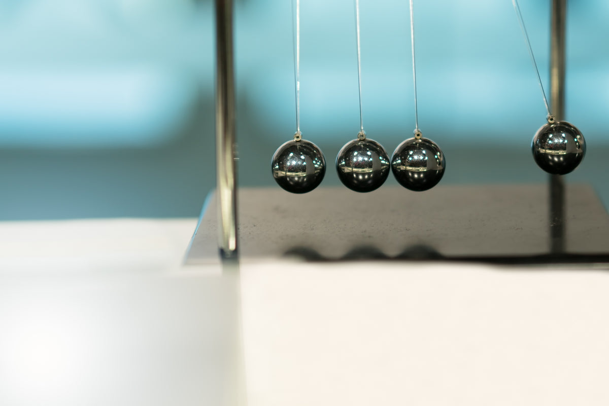 Metallische Newtonpendel auf schwarzem Sockel vor blauem Hintergrund