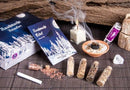Ein Rauhnacht-Ritualset mit Begleitheft, Räucherschale, Kerze und verschiedenen kleinen Glasfläschchen mit Kräutern und Harzen auf einer dunklen Matte.