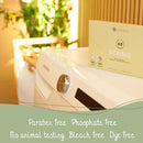 Eine Schachtel umweltfreundlicher Waschmitteltücher auf einer Waschmaschine, umgeben von sanftem Sonnenlicht. Texthervorhebungen: parabenfrei, phosphatfrei, tierversuchsfrei, bleichmittelfrei, farbstofffrei. Frischer und beruhigender Ton.