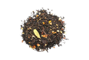 A pile of dark loose-leaf black magic blend tea with orange and brown spices and a green cardamom pod nestled among the leaves