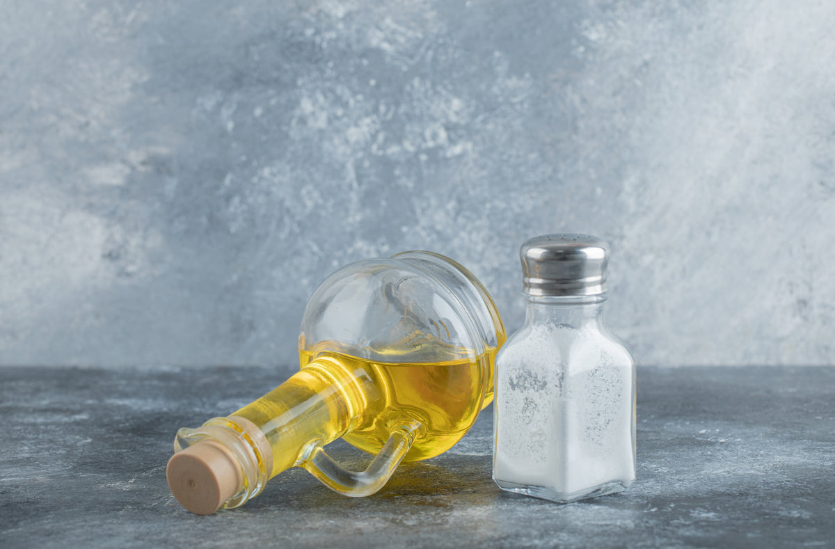 Glasflasche mit Olivenöl und ein Salzstreuer auf grauem Steinhintergrund