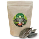 Ein Standbodenbeutel Ancient Purity Soursop Leaves (20g/0.7oz e) mit einem runden Etikett, das den Soursop-Baum, Früchte und eine dampfende Schale Tee zeigt. Unten liegen einige getrocknete Soursop-Blätter.
