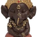 Nahaufnahme einer meditierenden dunkelbraunen Ganesha-Statue mit goldener Krone und Schmuck.