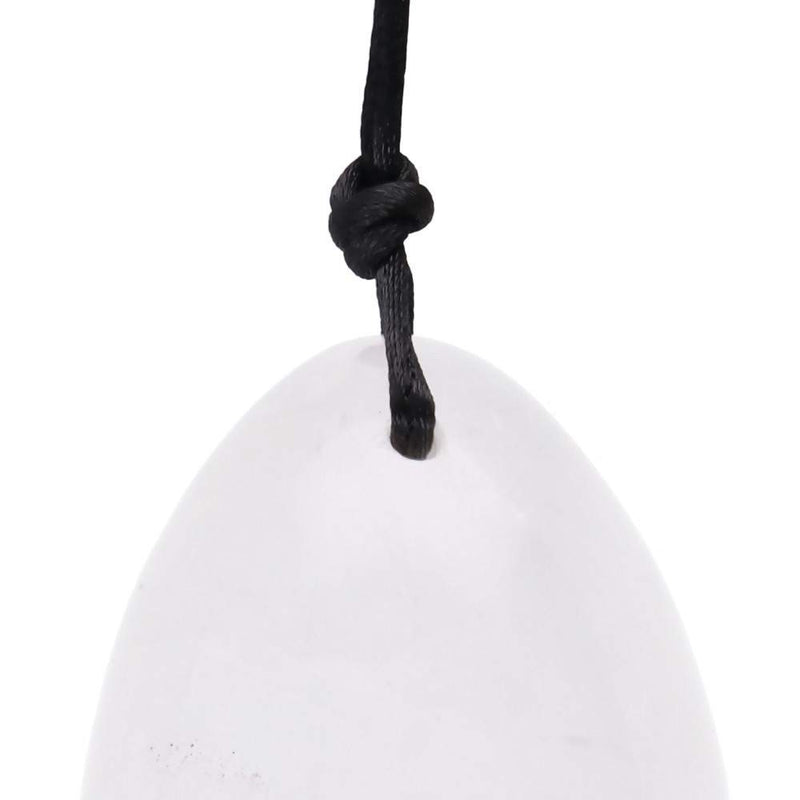 Nahaufnahme eines polierten, glatten, weißen oder klaren Kristall-Ei-Anhängers, der die Oberseite zeigt, durch die eine schwarze Kordel geknotet ist.