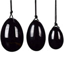 Ein Set aus drei glatten, polierten schwarzen Steineiern in verschiedenen Größen, die jeweils an einer schwarzen Schnur hängen.