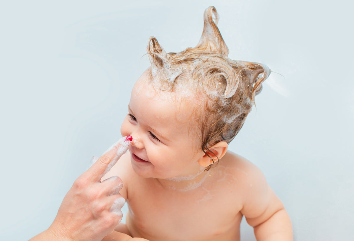 Lächelndes Baby beim Baden mit sanftem Bio-Shampoo und Schaum.