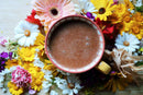 Ayamani Naturals Choc Me Up Adaptogener Cacao- und Mushroom-Mokka-Tee mit Reishi und Chaga, in einer Tasse auf einem Holzbrett.