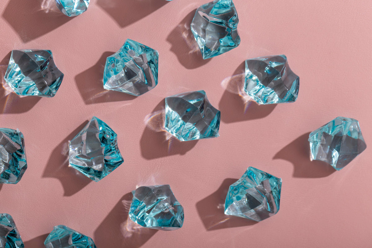 Dekorative hellblaue Glassteine mit Lichtreflexen auf rosa Hintergrund