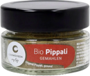Ein klarer rundglasbehälter mit schwarzem deckel enthält gemahlenes bio pippali von cosmoveda für ayurvedische küche