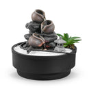Ein Desktop-Zen-Garten mit einem dreistufigen Wasserbrunnen, weißem Sand und einer Steinlaterne auf weißem Hintergrund.