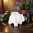 Ein weißer keramischer Elefanten-Ölbrenner auf einer Holzoberfläche mit lila Blumen.