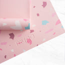 Eine Makro-Nahaufnahme einer rosa Yogamatte mit Terrazzo-Muster, die das geprägte „myga“-Logo und die gerippte, rutschfeste Oberflächenstruktur zeigt.