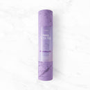 Eine eingerollte lila Myga Chakra Yogamatte mit Marmormuster und einer Papierhülle, auf der eine Yoga-Pose abgebildet ist.