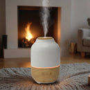Aroma-Diffusor aus Holz und weißer Keramik mit Licht und Dampf vor einem leuchtenden Kamin.