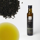 Eine Flasche Schwarzkümmelöl (Oleum Nigella sativa) von Ölwerk steht rechts auf weißem Grund, mit einem Haufen tiefschwarzer Schwarzkümmelsamen oben links und einem verschwommenen Tropfen des leuchtend gelben Öls unten links. Das Etikett der Flasche bewirbt "feinste biologische Öle" und "100% rein & naturbelassen".