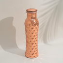 Eine einzelne, hohe, glänzende Kupfer-Trinkflasche mit Wabenstruktur oder gehämmertem Muster, vor einem weißen Hintergrund mit einem schwachen Blattschatten.