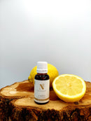 Eine kleine Flasche Zitronenöl auf einer Holzscheibe neben frischen ganzen und halbierten Zitronen.