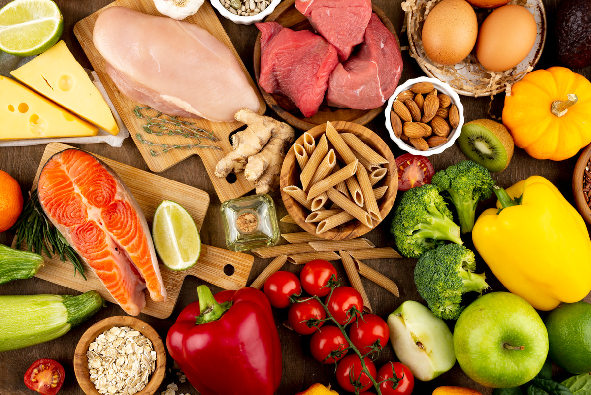 Frische Bio-Lebensmittel mit Lachs, Fleisch, Gemüse, Eiern und Vollkornpasta auf Holz.