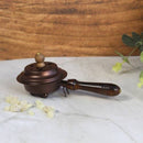 Eine Hand, die den Deckel eines Weihrauchgefäßes über den Kupfersockel hält und dabei das Innere sowie den Holzgriff zeigt.