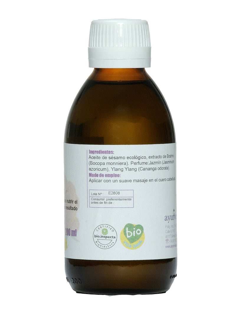 Dunkle Glasflasche mit weißem Deckel und weißem Etikett. Das Etikett listet Inhaltsstoffe wie Bio-Sesamöl und Brahmi-Extrakt sowie Anwendungshinweise für die Kopfhautmassage auf.
