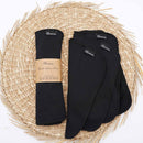 Gerollte und gefaltete schwarze, wiederverwendbare Küchentücher mit Etiketten, auf einer runden, gewebten Strohmatte.