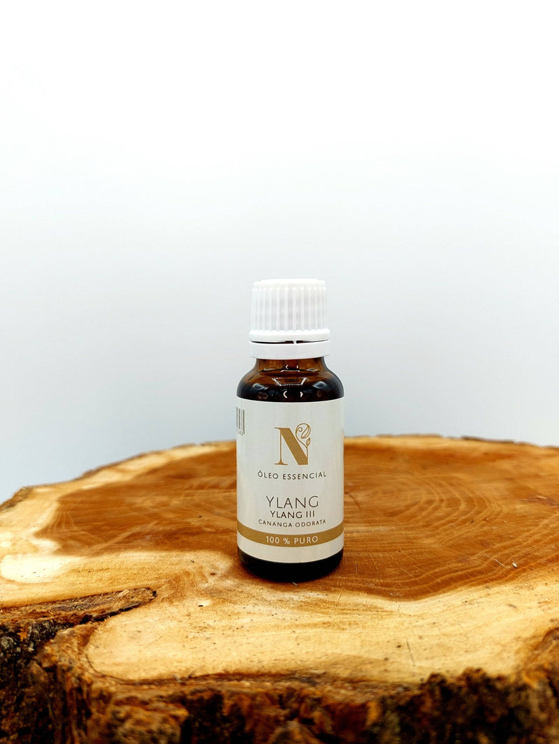 Kleine Flasche Ylang-Ylang-Öl auf einer strukturierten Holzscheibe.